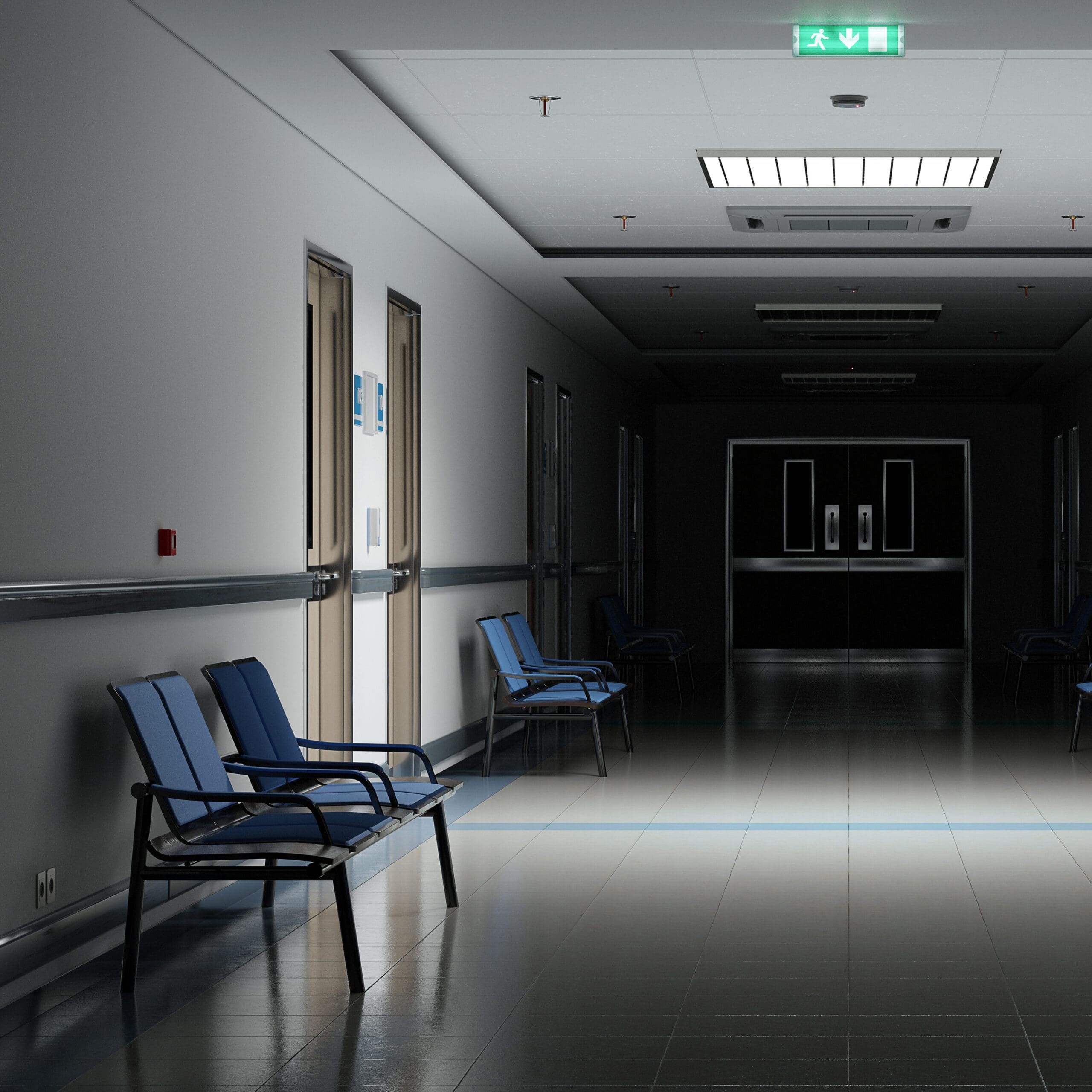 A dimly lit hospital hallway with blue chairs lined up along the wall. The corridor is empty, and the floor is reflective. Bright emergency exit sign is visible on the ceiling, and doors lead to rooms on the left.
